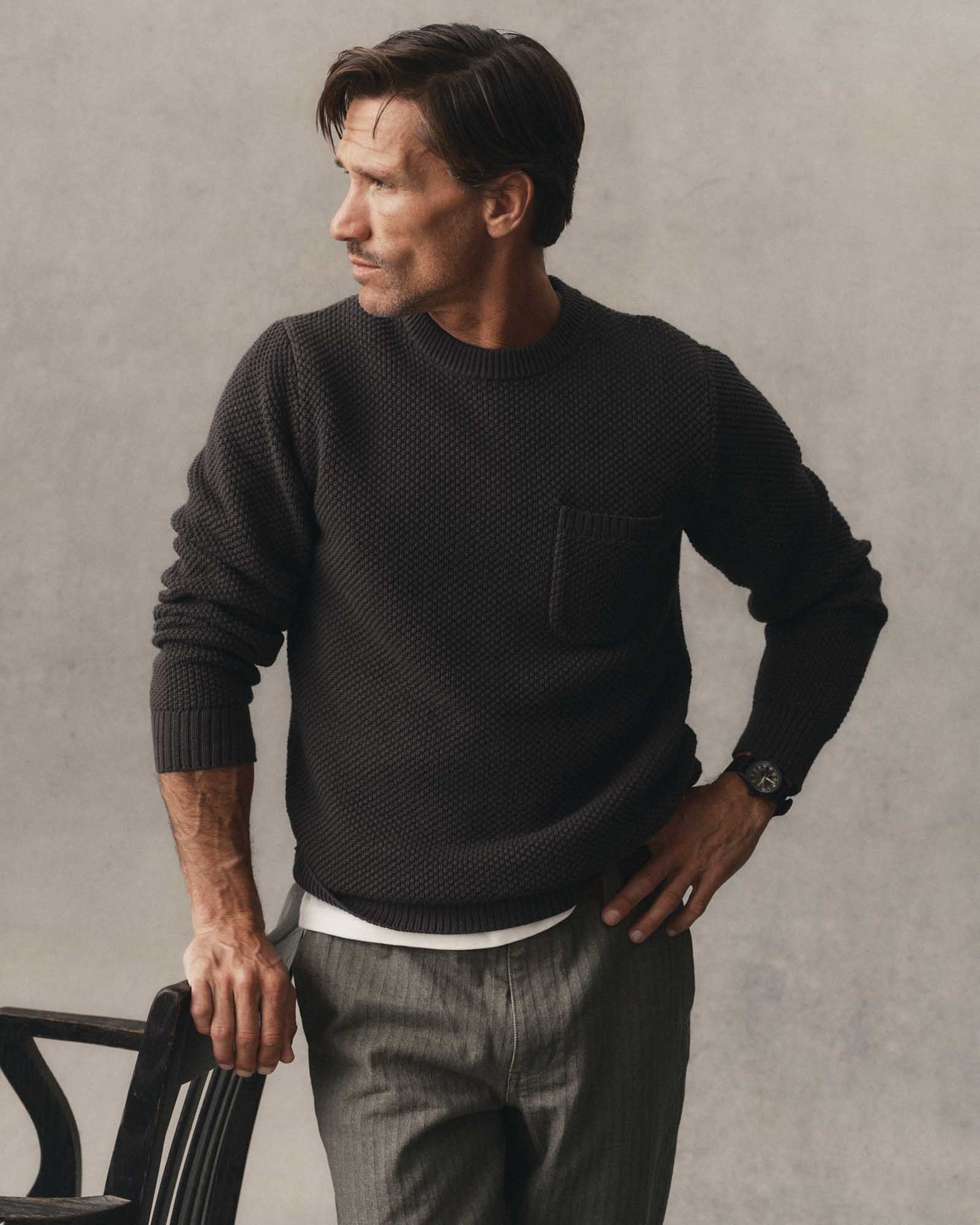 fit model leaning against a chair wearing The Crawford Crew Sweater in Charcoal, Sweaters by Taylor Stitch
