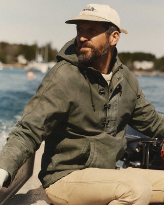 fit model sitting wearing The Hatteras Anorak in Fatigue Olive Dry Wax Canvas