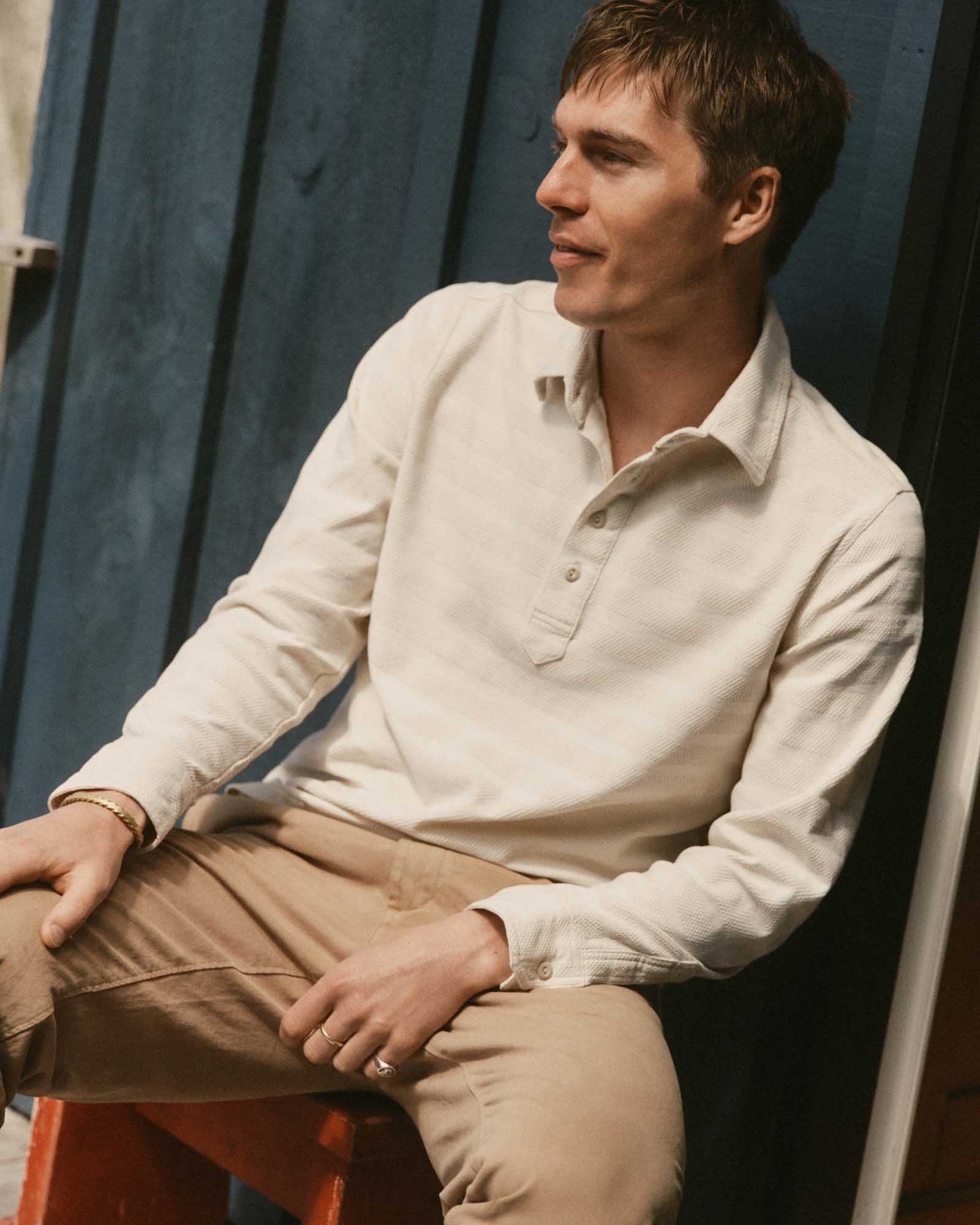 fit model sitting wearing The Long Sleeve Polo in Vintage White Knit Stripe, Knits by Taylor Stitch