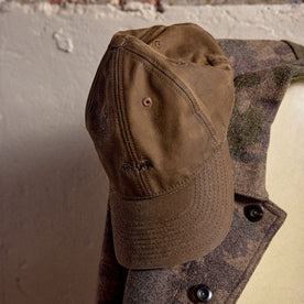 The Ball Cap in Dark Khaki Waxed Canvas hanging on a coat
