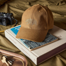 The Ball Cap in Tobacco Canvas on a stack of books