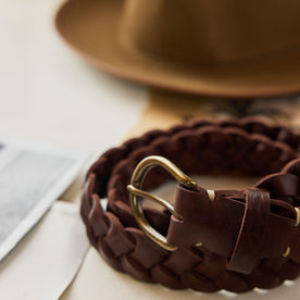 The Braided Belt in Dark Brown next to a hat