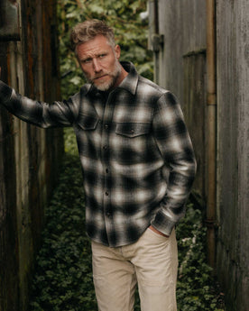 fit model leaning on the wall wearing The Maritime Shirt Jacket in Olive Plaid, Wovens by Taylor Stitch