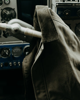 editorial image of The Workhorse Jacket in Stone Chipped Canvas hanging off of a seaplane wheel, Outerwear by Taylor Stitch