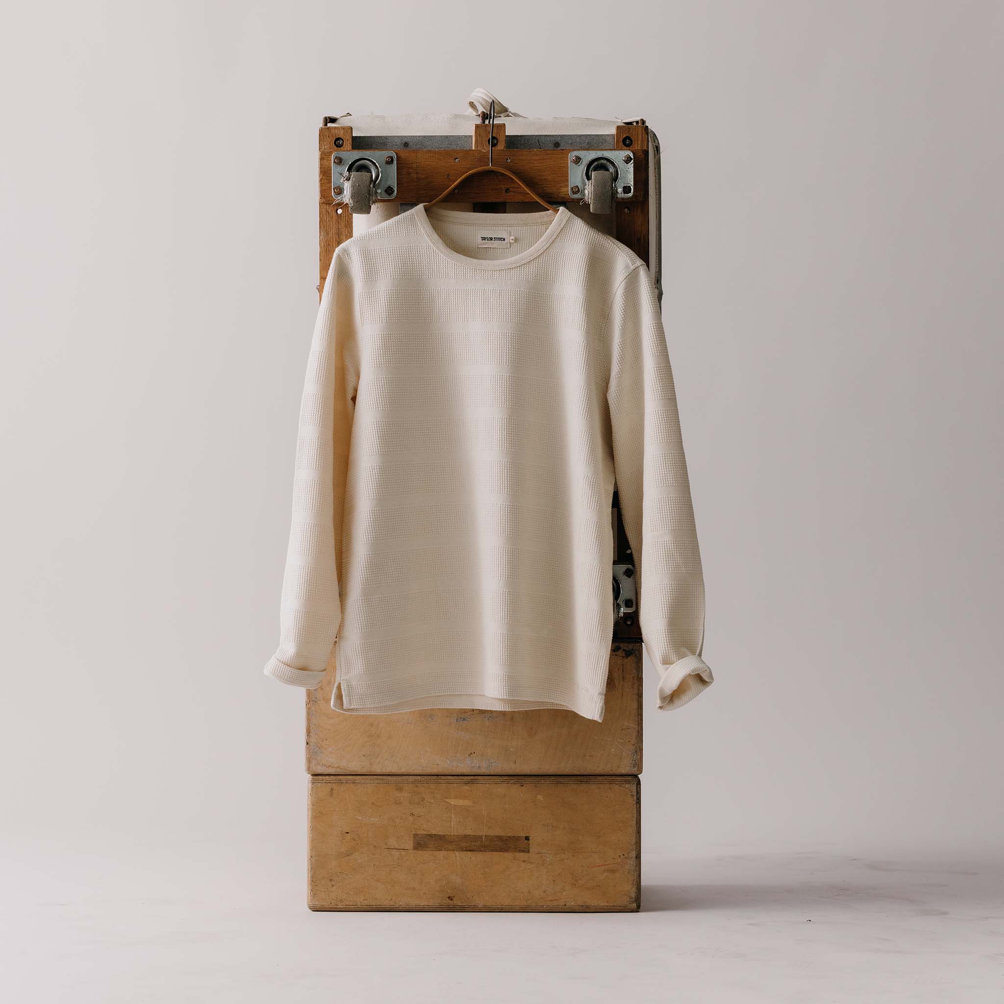 editorial image of The Morgan Crewneck in Natural Slub Stripe on a hanger on a trunk, Knits by Taylor Stitch