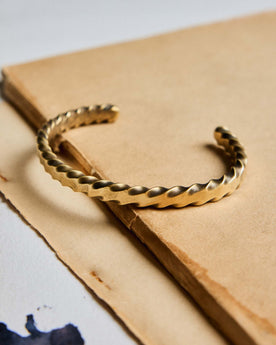 editorial image of The Twisted Cuff in Brass on a piece of paper, Accessories by Taylor Stitch