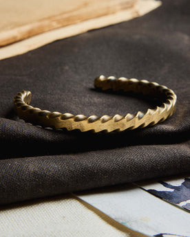 editorial image of The Twisted Cuff in Brass on a piece of fabric, Accessories by Taylor Stitch