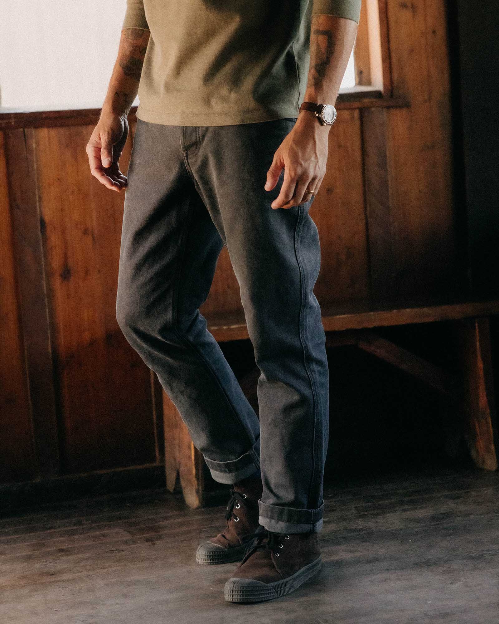 fit model leaning against a wood pile wearing The Camp Pant in Coal Chipped Canvas, Bottoms by Taylor Stitch