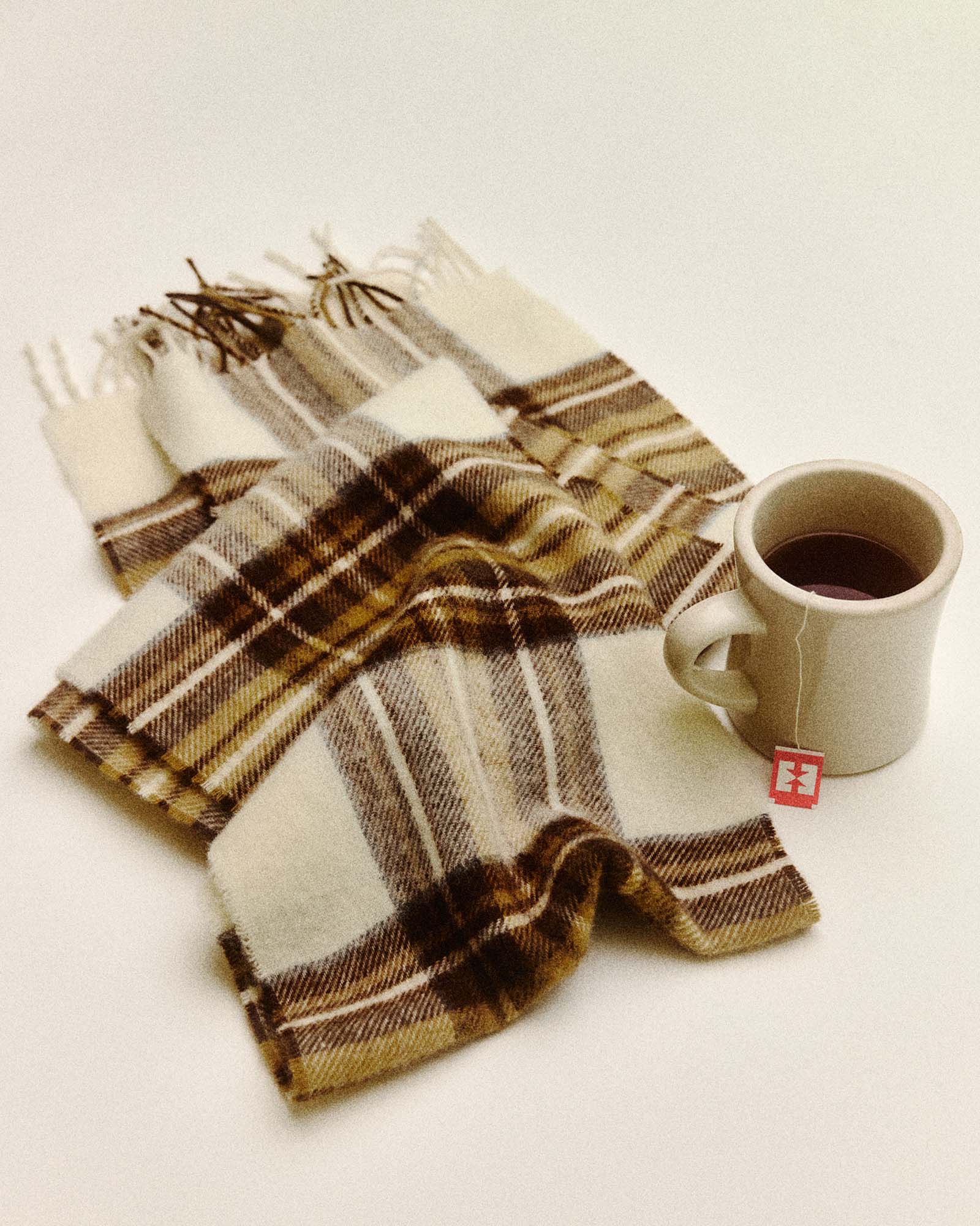 editorial flatlay of The Fireside Scarf in Butterscotch Plaid next to a cup of tea, Accessories by Taylor Stitch