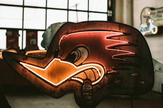 A vintage orange and yellow neon sign featuring an angry bird with cigar stub in its mouth. 