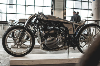 A retro-mod motorbike displayed in a brightly-lit space, with people walking behind looking at other displays.