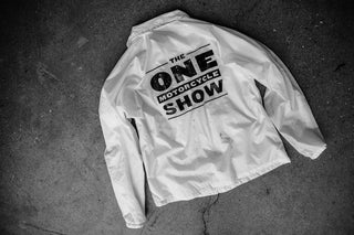 Overhead shot of the reverse 'The One Motorcycle Show'-printed white jacket on a black floor.