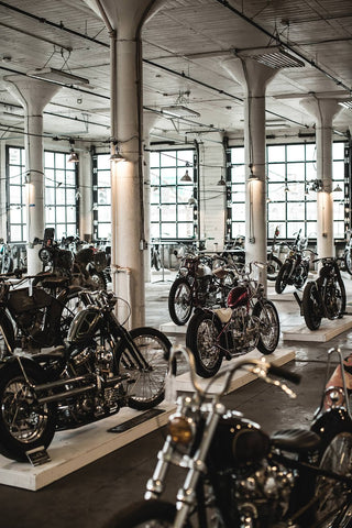 Wide shot of a well-lit windowed space, featuring several vintage motorcycles on display.