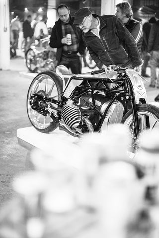 Blurred black and white image of two men looking over a motorbike on display.