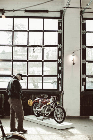 An older gentleman studying a vintage motorbike in a very well lit wide angle shot.