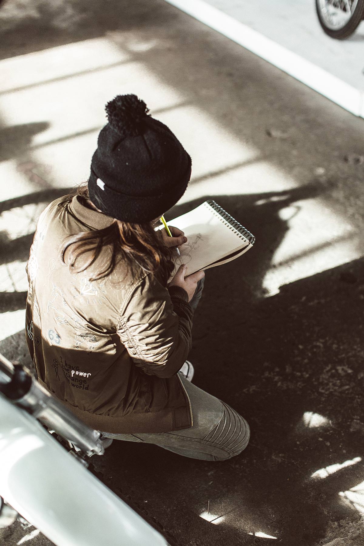 Over the shoulder view of someone sketching a displayed motorcycle.