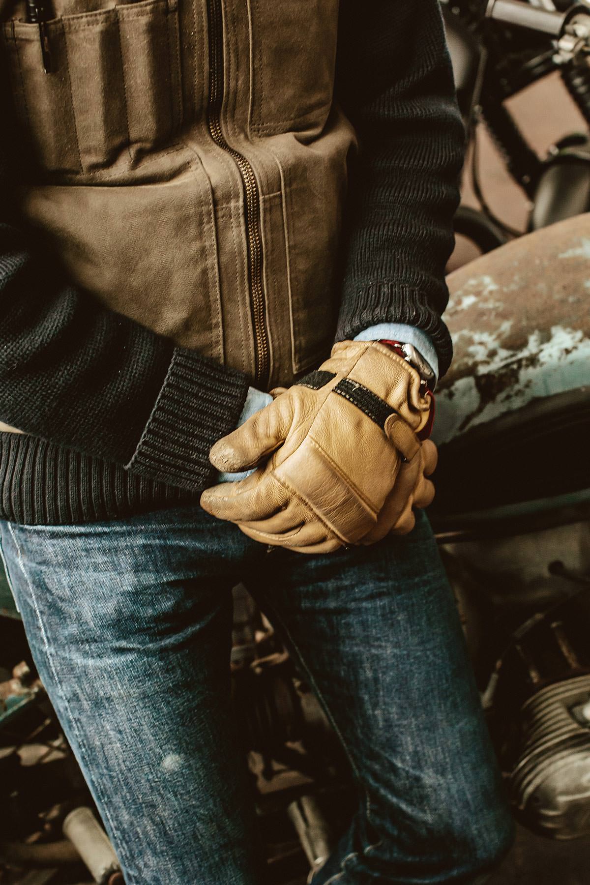 Cropped image of a man sitting on a parked motorcycle, wearing leather gloves, hands folded in lap.