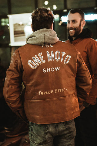Two gentlemen talking, both wearing One Moto Show-branded leather jackets over hooded sweatshirts.