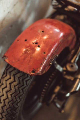 Close up on a beat-up red rear fender and motorcycle tire.