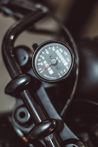 Close-up shot of the speedometer/odometer mounted on a motorcycles handlebars.