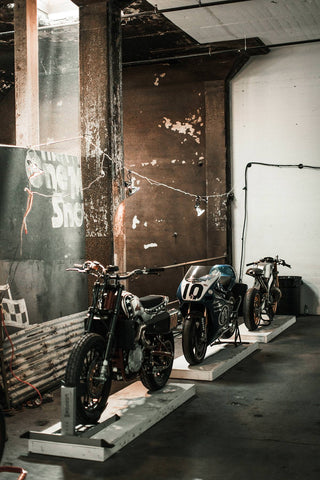 Three vintage motorcycles mounted for display in an industrial setting.