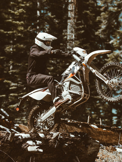 A moto rider pulling a wheelie to hop over a grounded tree trunk.