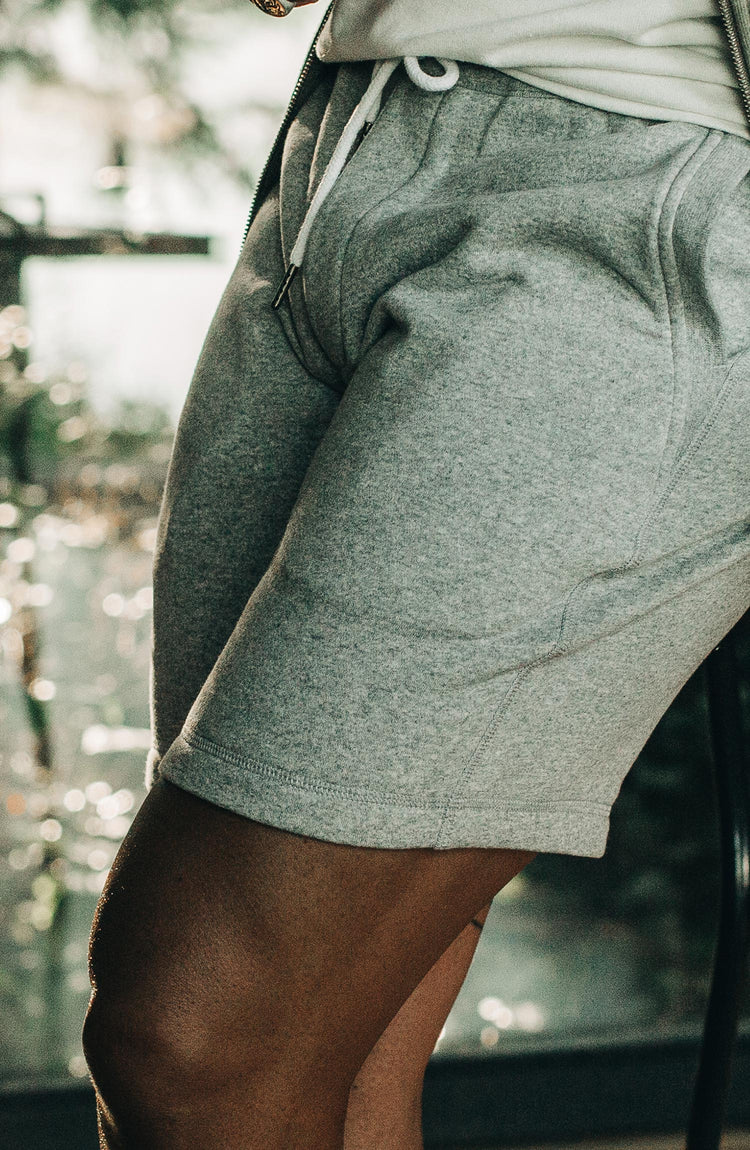 The Heavy Bag Short in Heather Grey Fleece — Diptych of model closeups while leaning up against table