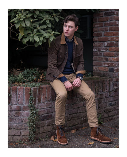 John perched on an old brick wall, with foliage in the background.