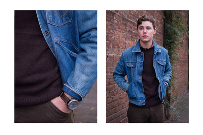 John rocking our sweater under a denim jacket, shot against an old brick wall.