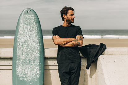 Model wearing The Merino Tee next to a surfboard