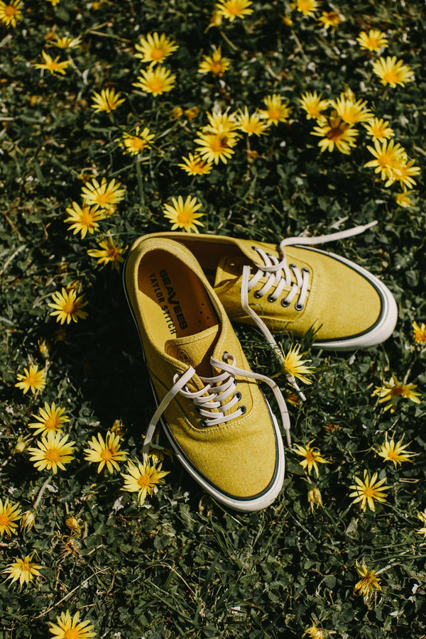 Shot of the gold Vista sneakers in the grass with yellow flowers.