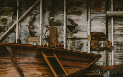 A well-used boat shed with tools and bows of a wooden row boat in the foreground.