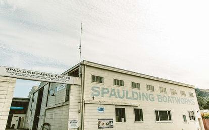 A white-washed wooden building with 'Spaulding Boatworks' painted on its side in large light-blue letters.