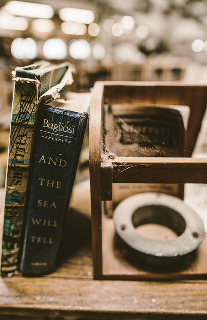 Close-up shot of a dusty bookshelf, with 'And The Sea Will Tell' by Bugliosi.