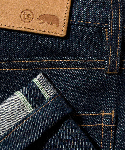 Details on folded denim jeans: leather patch, belt loops, hem, pocket corner.