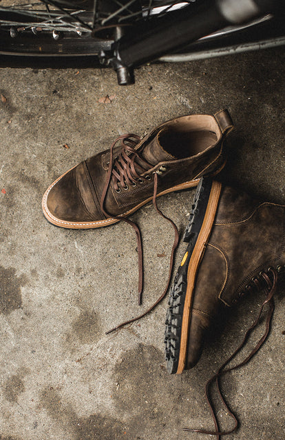 A pair of unlaced boots on the ground next to a motorcycle.