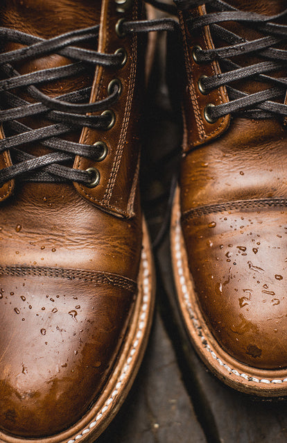 Close-up cropped shot of boots, with water pooling on the waterproof leather.