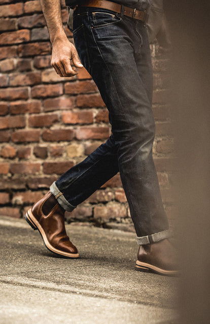 Lower legs, wearing denim and boots, walking down a brick-lined sidewalk.