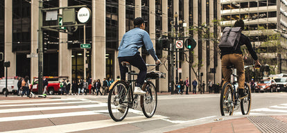 Two friends riding e-bikes away from camera down Market St in downtown SF.