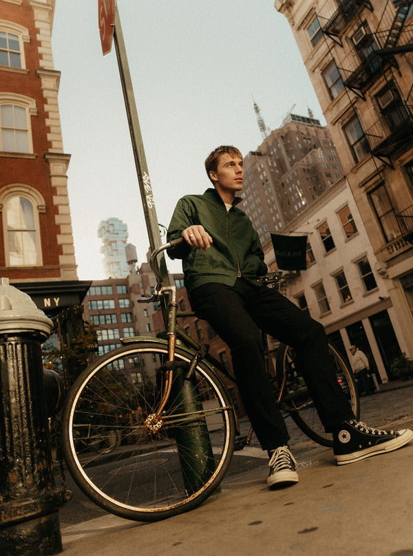 Model resting on a city bike, wearing The Dean Jacket