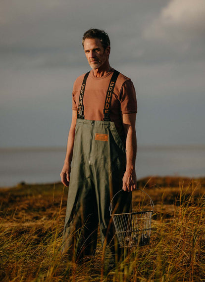 Model wearing The Rugby Tee in Faded Brick, holding a bucket of oysters