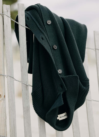 The Harbor Sweater Jacket in Black Pine Heather draped over a fence
