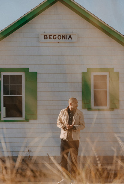 Model wearing a Flint Jacket, standing in front of a saltbox house