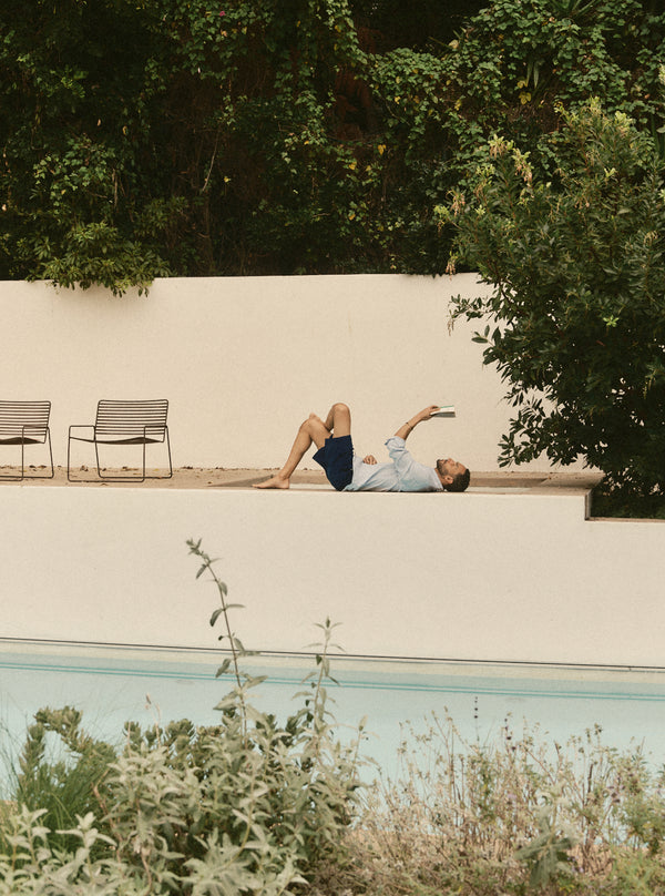 Model lying down and reading by the poolside