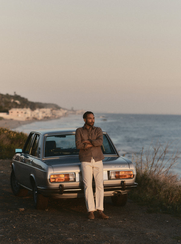 Model standing by a vintage BMW, watching the sunset over the coast