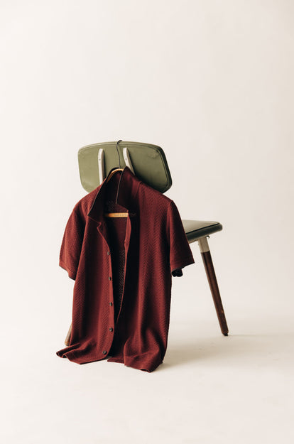 The Button Down Polo in Dried Cherry Herringbone, hanging from the back of a chair