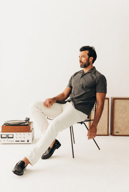 Model sitting on a chair in The Davis Shirt in Kelp Stripe
