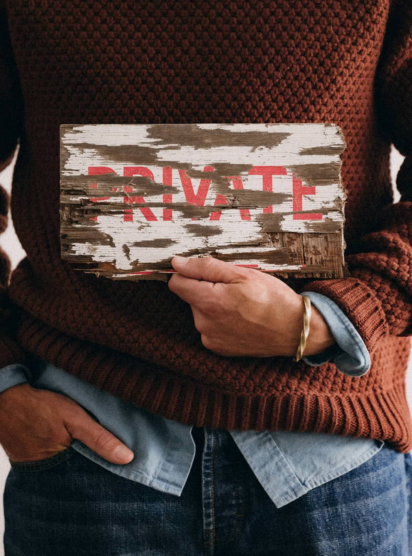 Model holding up a sign, wearing the Fisherman Sweater in Heather Brick Merino