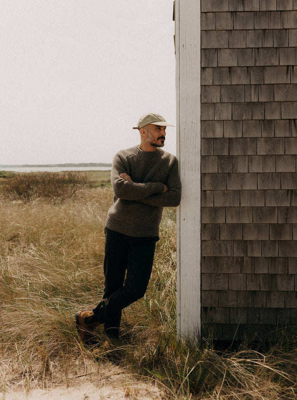 Model leaning against a cabin wall, wearing The Fisherman Sweater