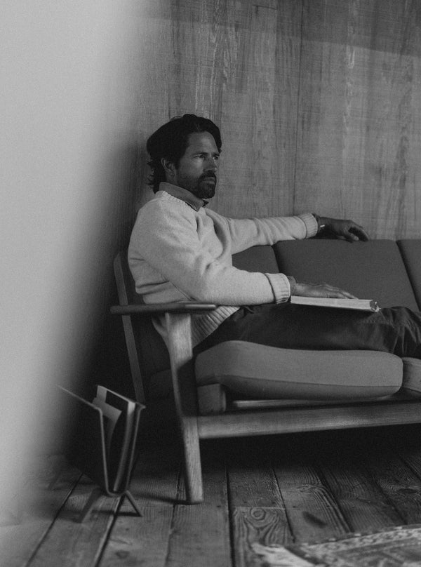 Model sitting on a couch wearing The Eastmoor Sweater